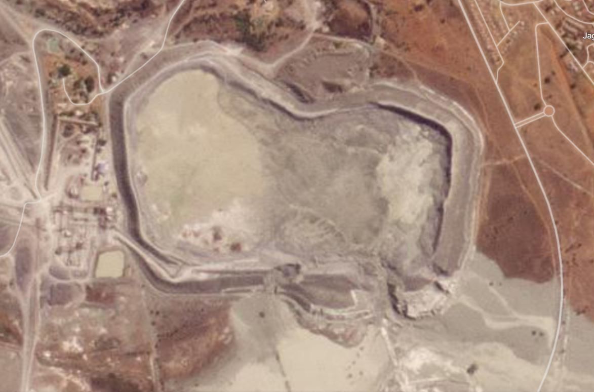 Aerial view of a large, dry, gray pit surrounded by earthen walls, possibly a quarry or mine.
