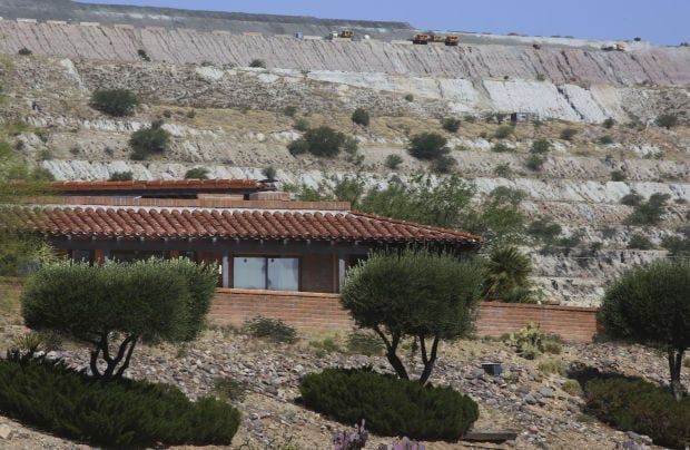 Homes with terracotta roofs in front of a layered, excavated hillside with sparse vegetation.