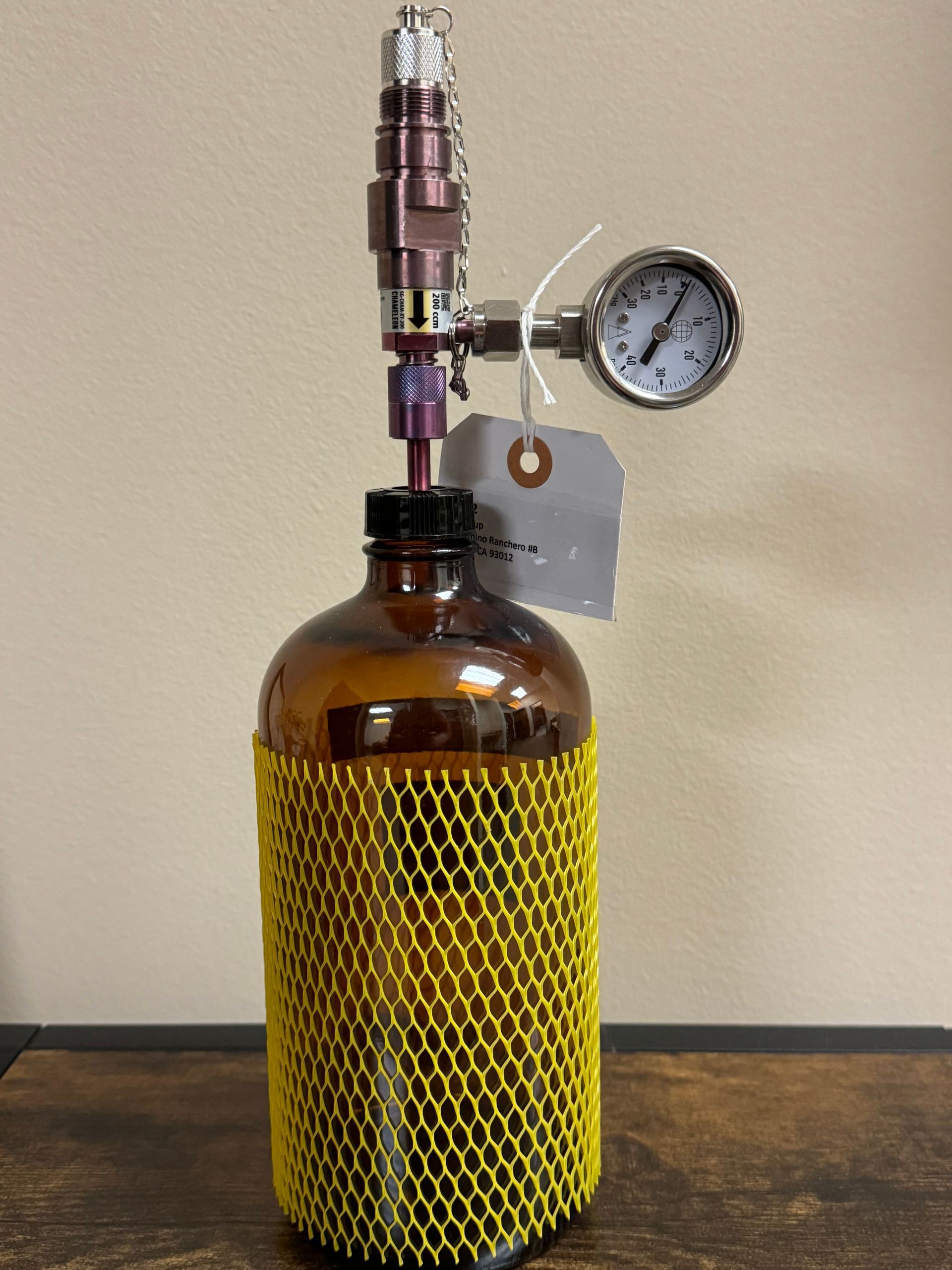 Amber glass bottle with purple and silver apparatus, pressure gauge, and yellow netting.