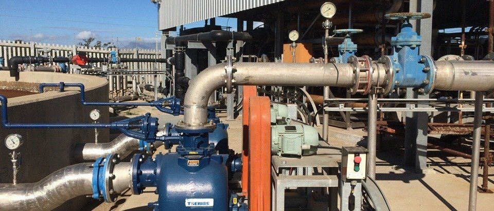 Complex industrial equipment with pipes, valves, and gauges outdoors under a bright sky.