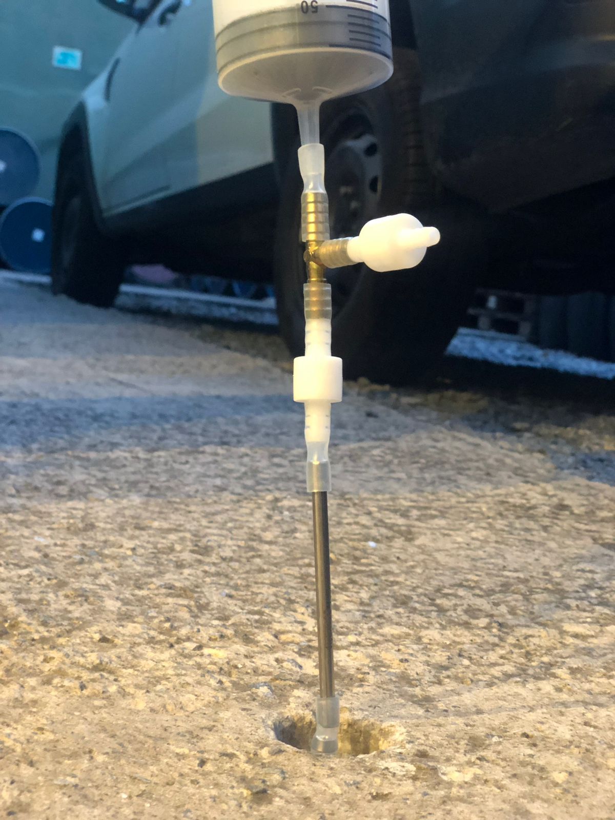 A device injecting a substance into a hole in concrete, near a car.