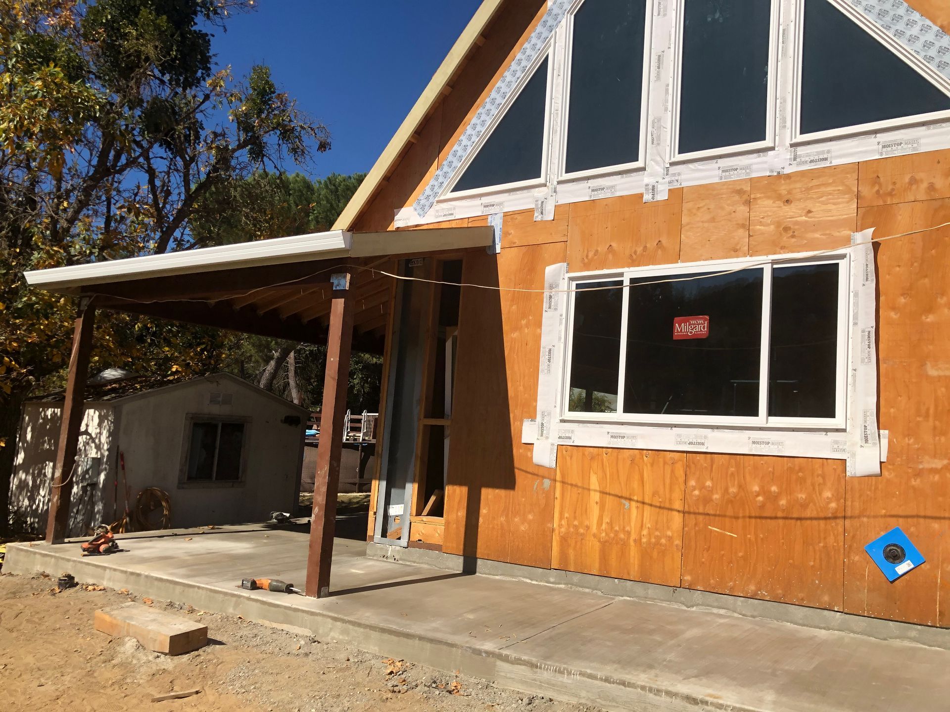 House under construction with porch, unfinished wood siding, and windows.