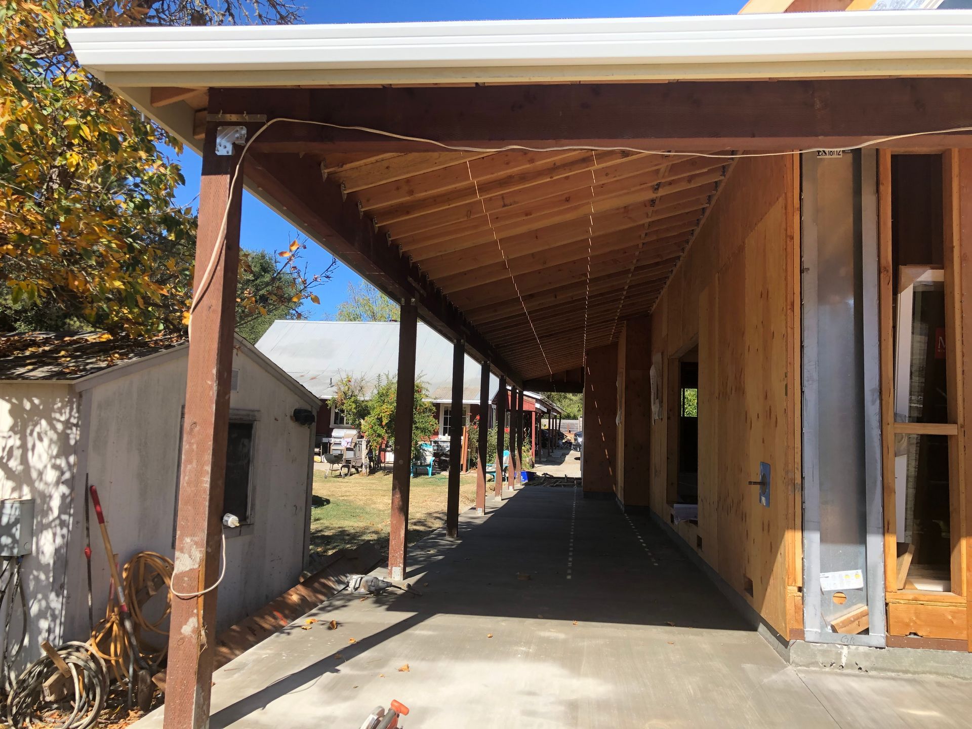 A covered walkway under construction with brown wooden beams and a concrete floor.