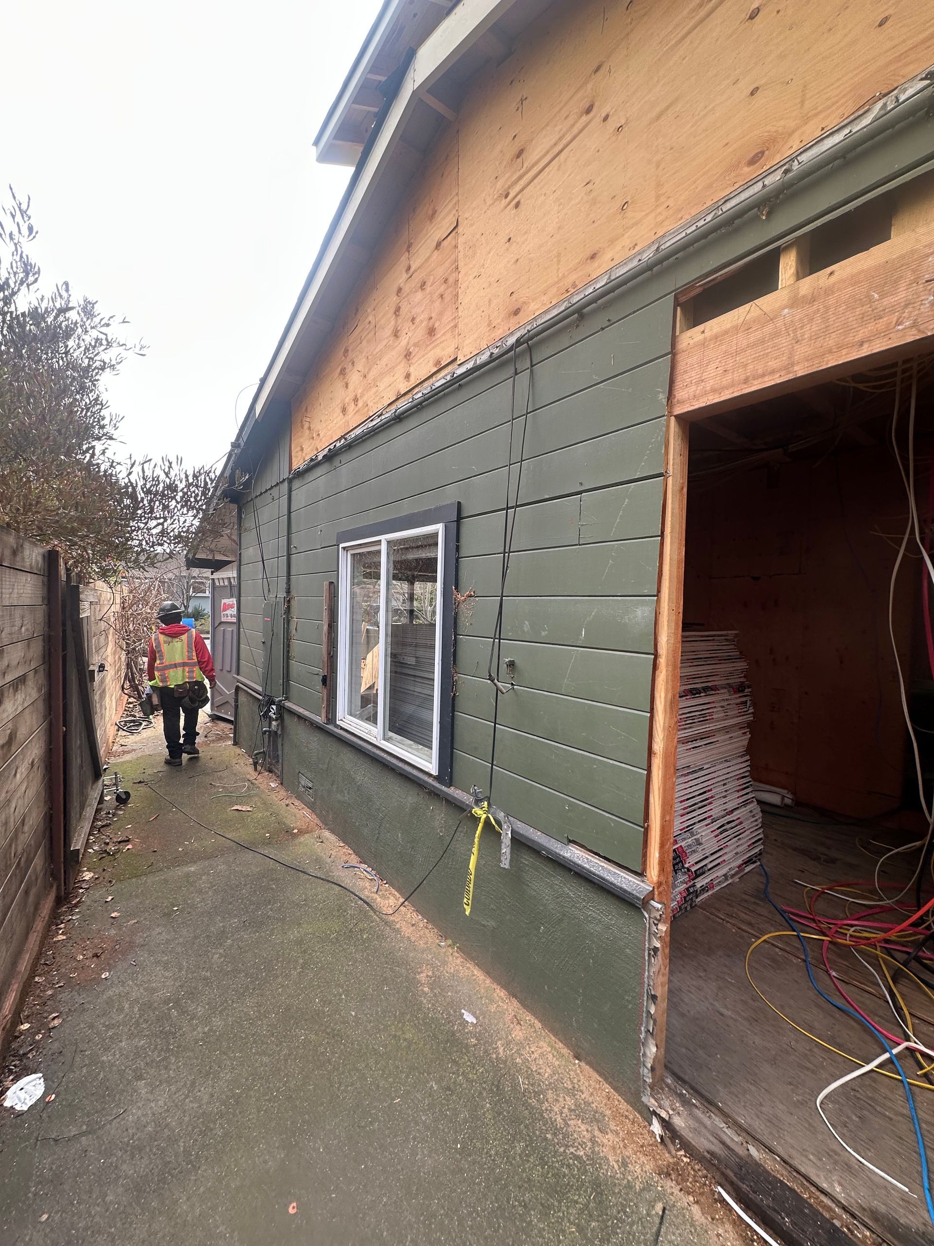 Side view of a building under construction, featuring olive green siding, a window, and an open doorway.
