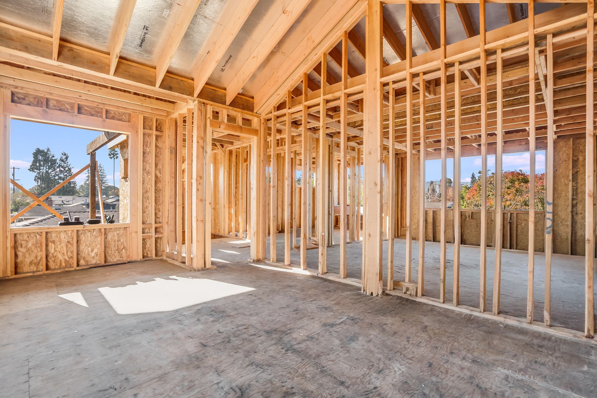 Interior framing of a house under construction with exposed wooden beams and concrete floor.