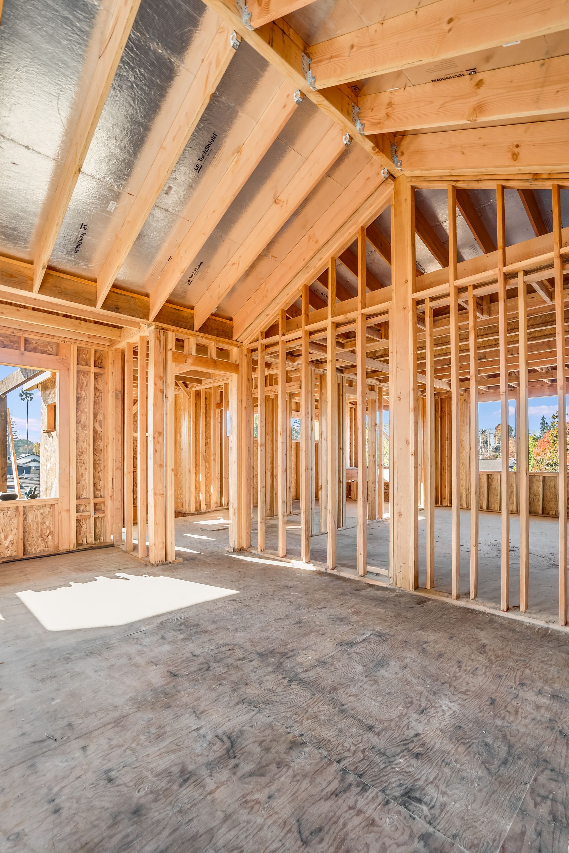 Interior view of a building under construction, framed with wooden beams and studs; gray concrete floor.