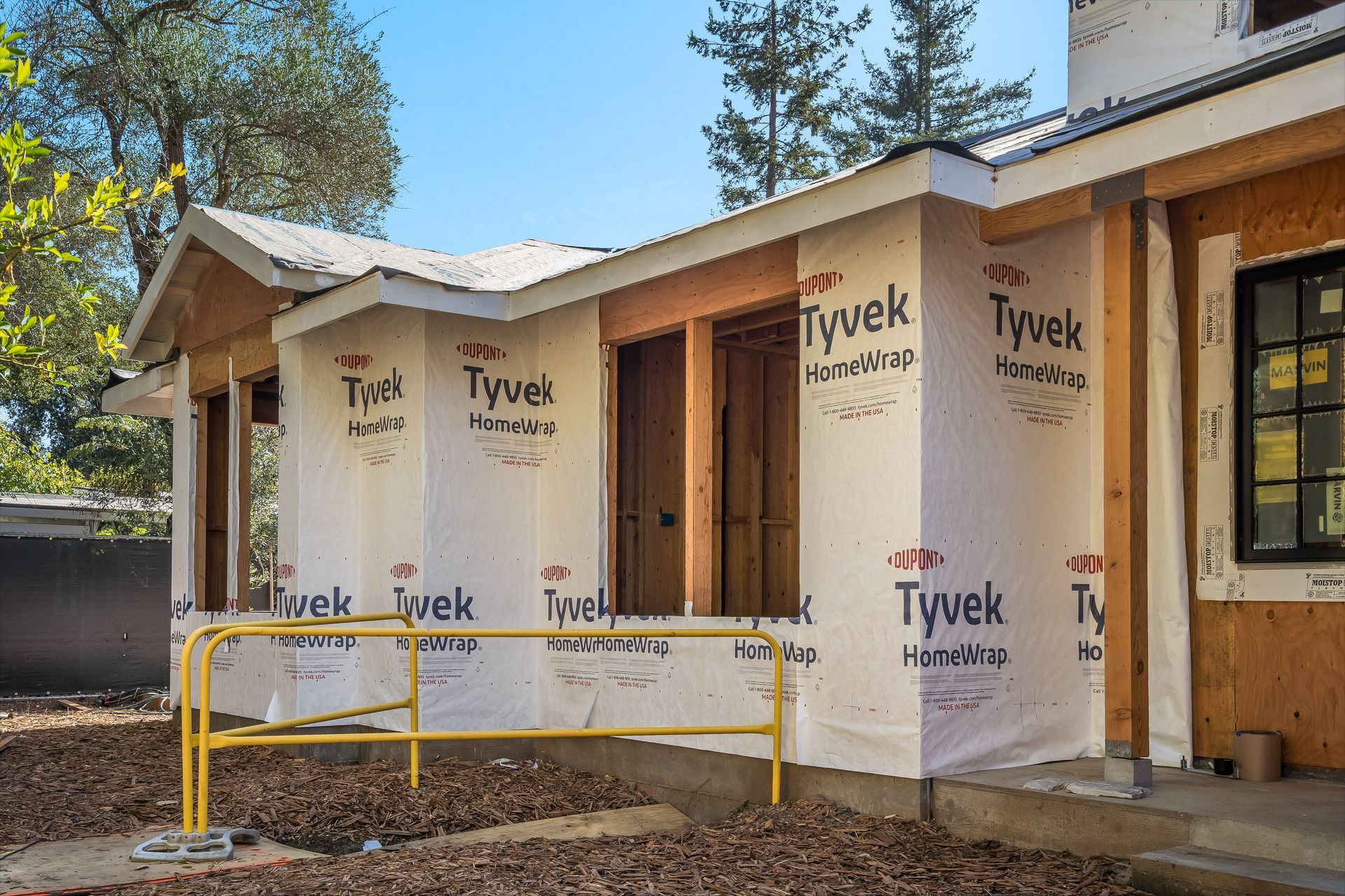 Construction site: House exterior with Tyvek wrap, open doorways, and yellow safety railing.