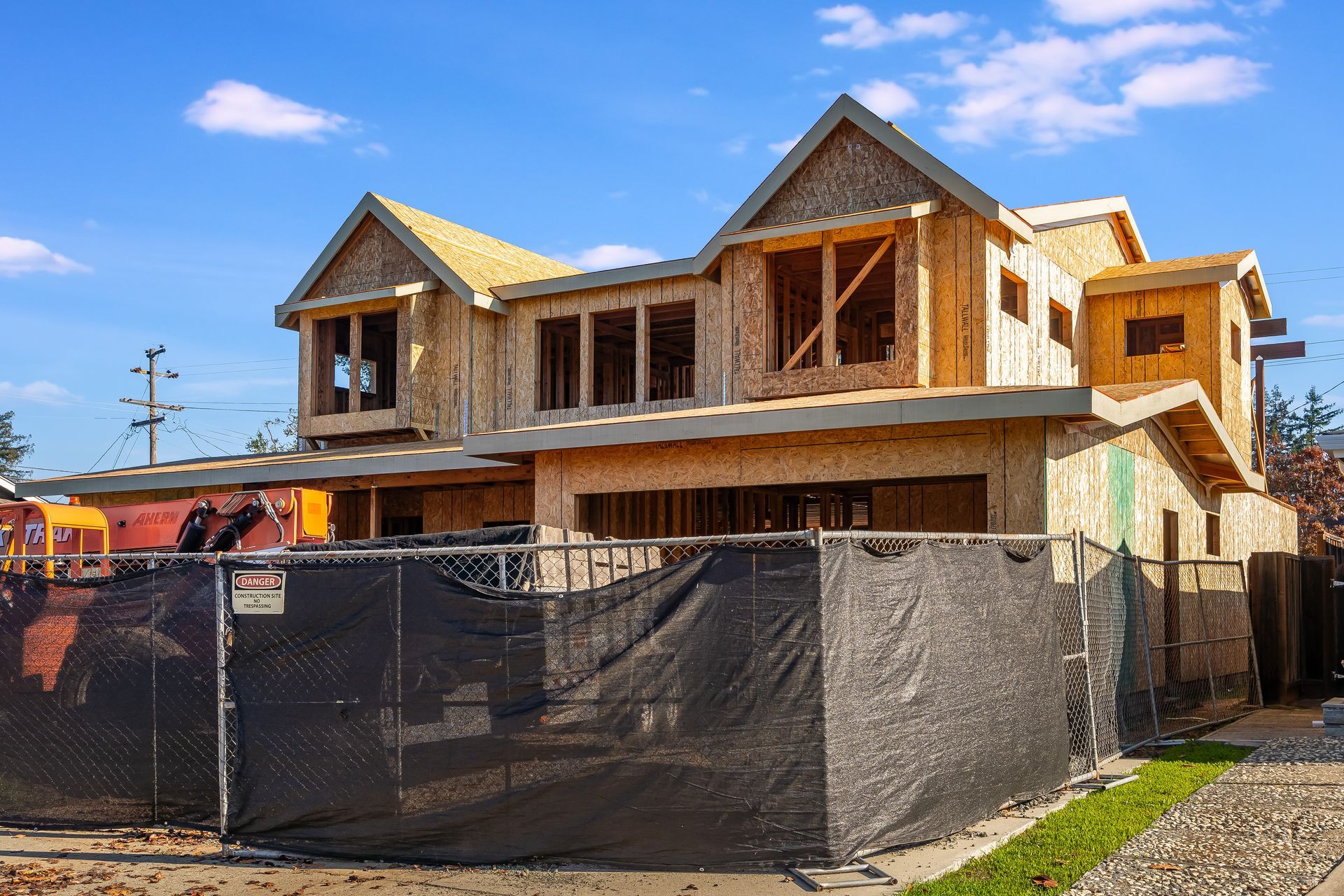 New house under construction, framed wooden structure with blue sky background behind a black fence.