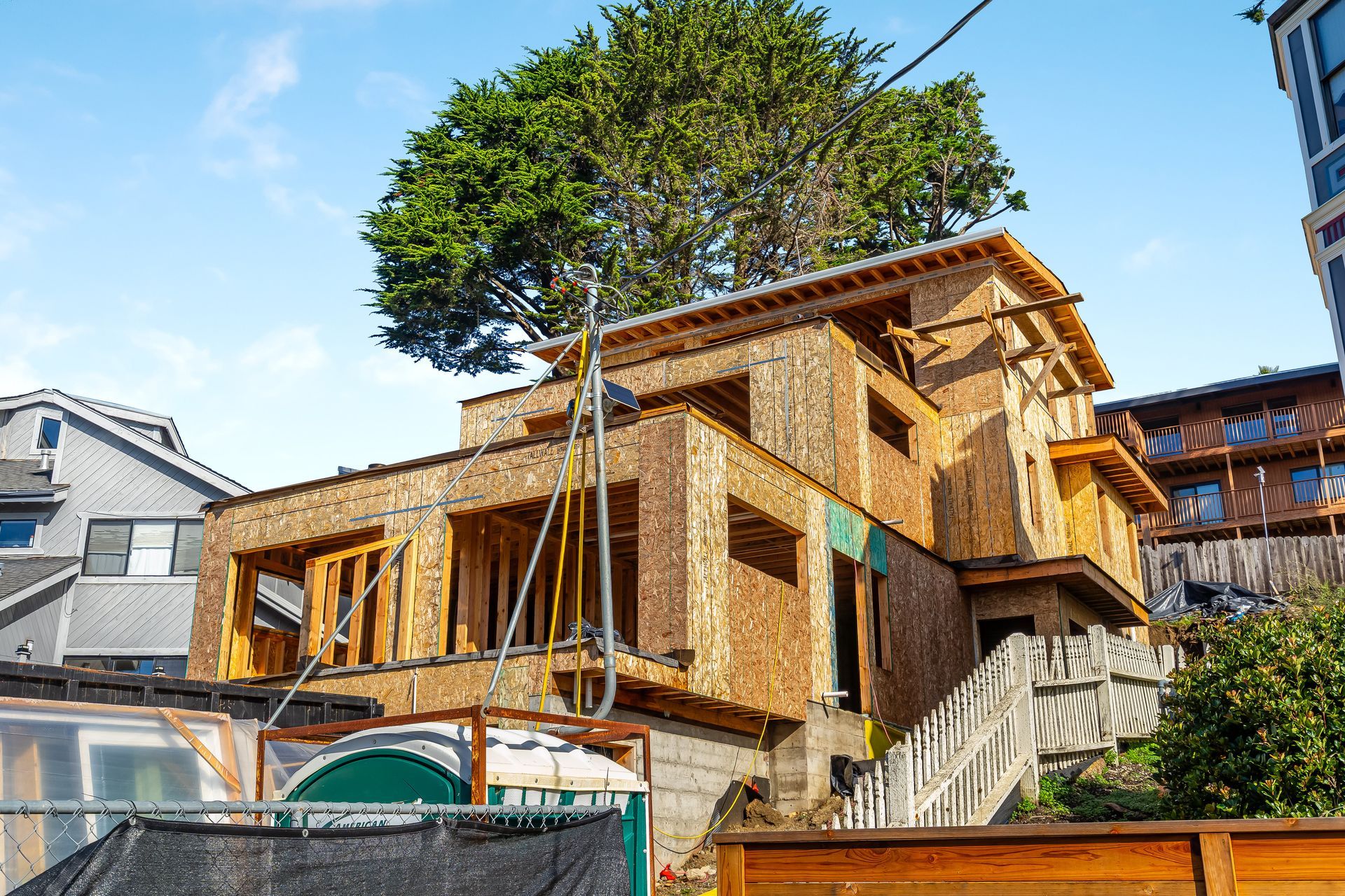Wood-framed house under construction on a hillside, sunny day.
