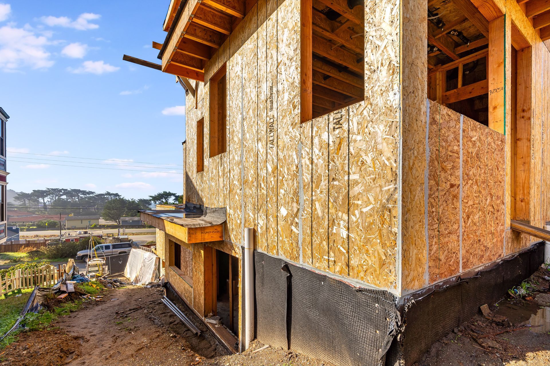 Construction of a two-story wood-framed building with OSB siding against a blue sky.