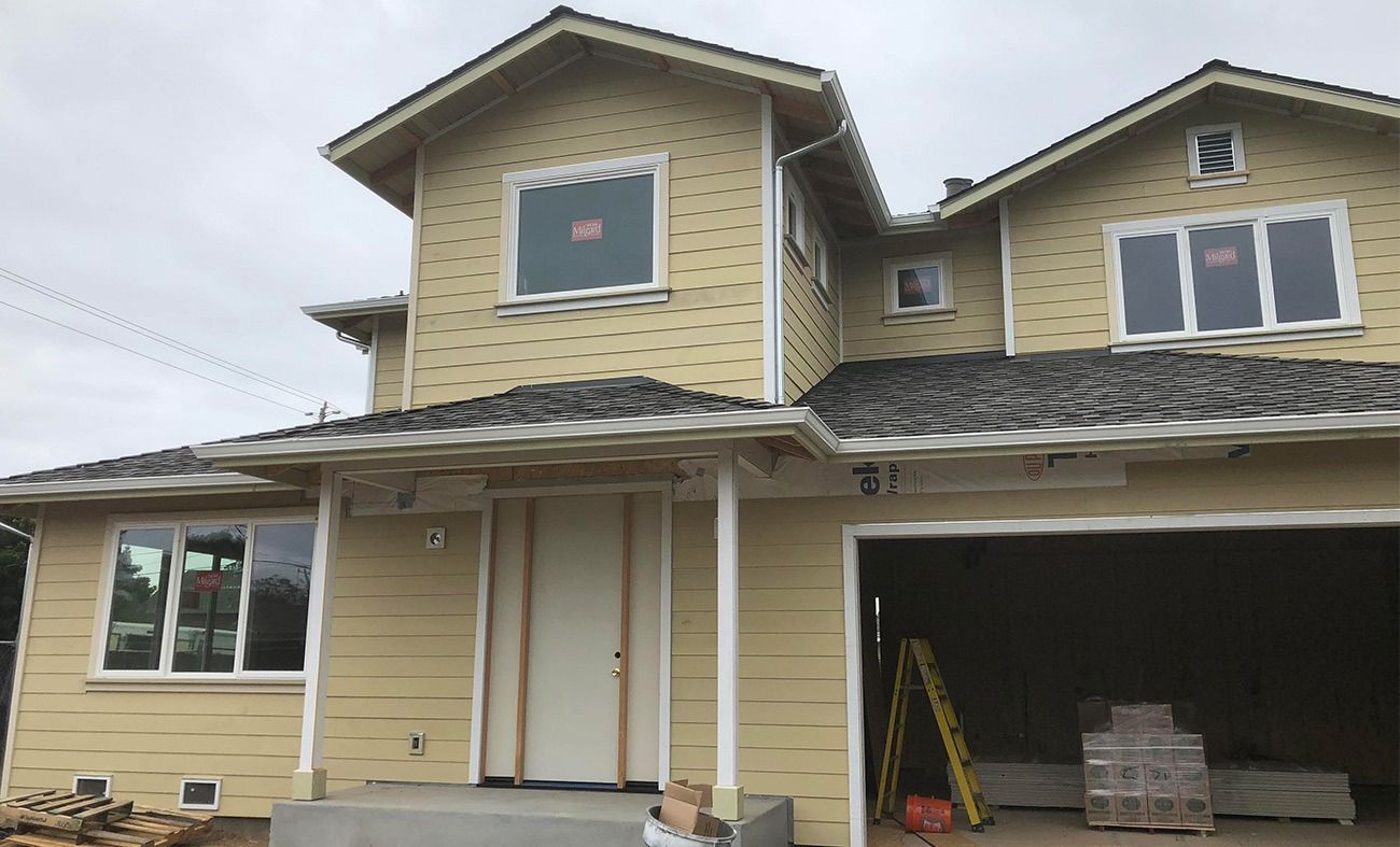 Two-story house under construction, yellow siding, white trim, gray roof, open garage, window and door frames.