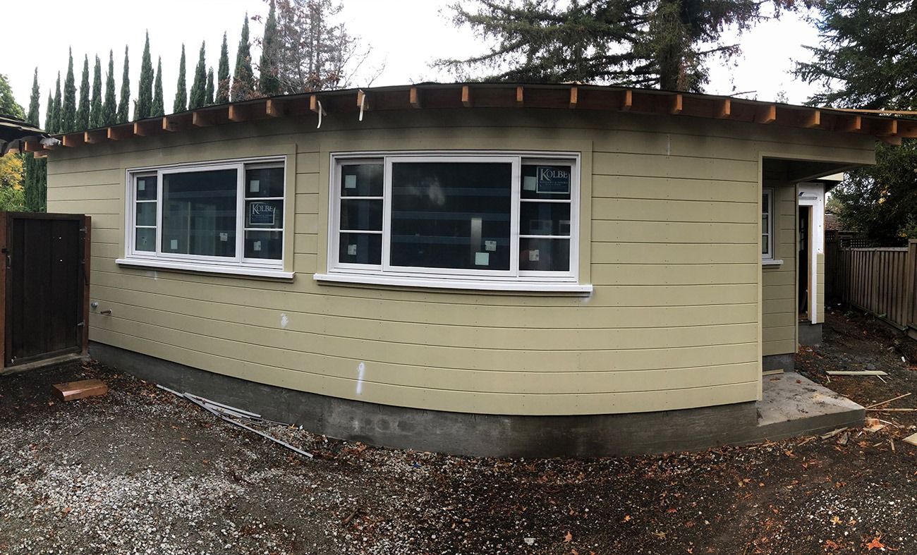 Beige shed with white-framed windows under construction, set in a yard.