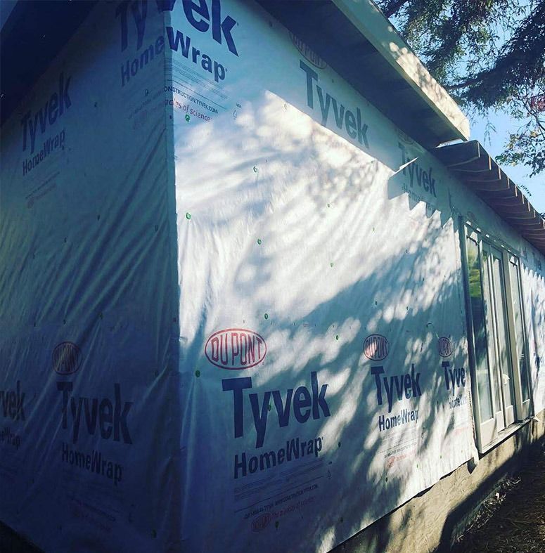 Building exterior wrapped in Tyvek HomeWrap, with windows visible along one wall, sunny setting.