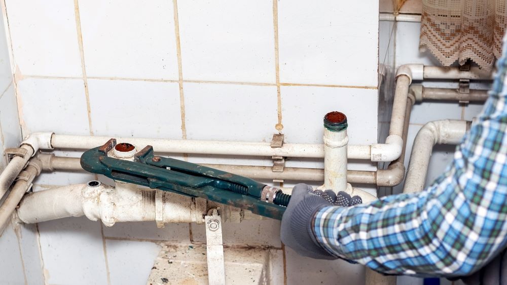 A Man is Fixing a Pipe With a Wrench in a Bathroom — Absolute Plumbing Australia in Howard Spring, NT