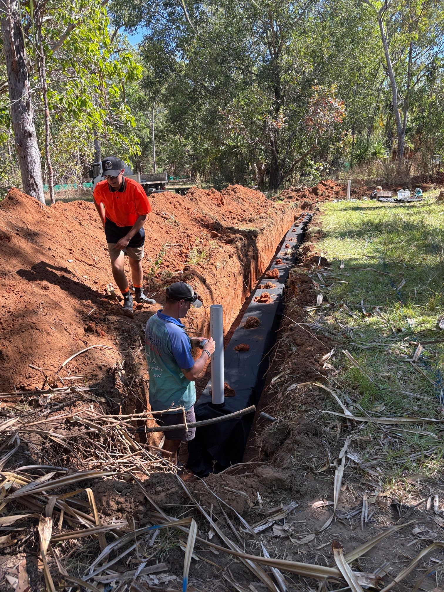 Two men are working on a pipe that is in the ground— Absolute Plumbing Australia in Howard Spring, NT