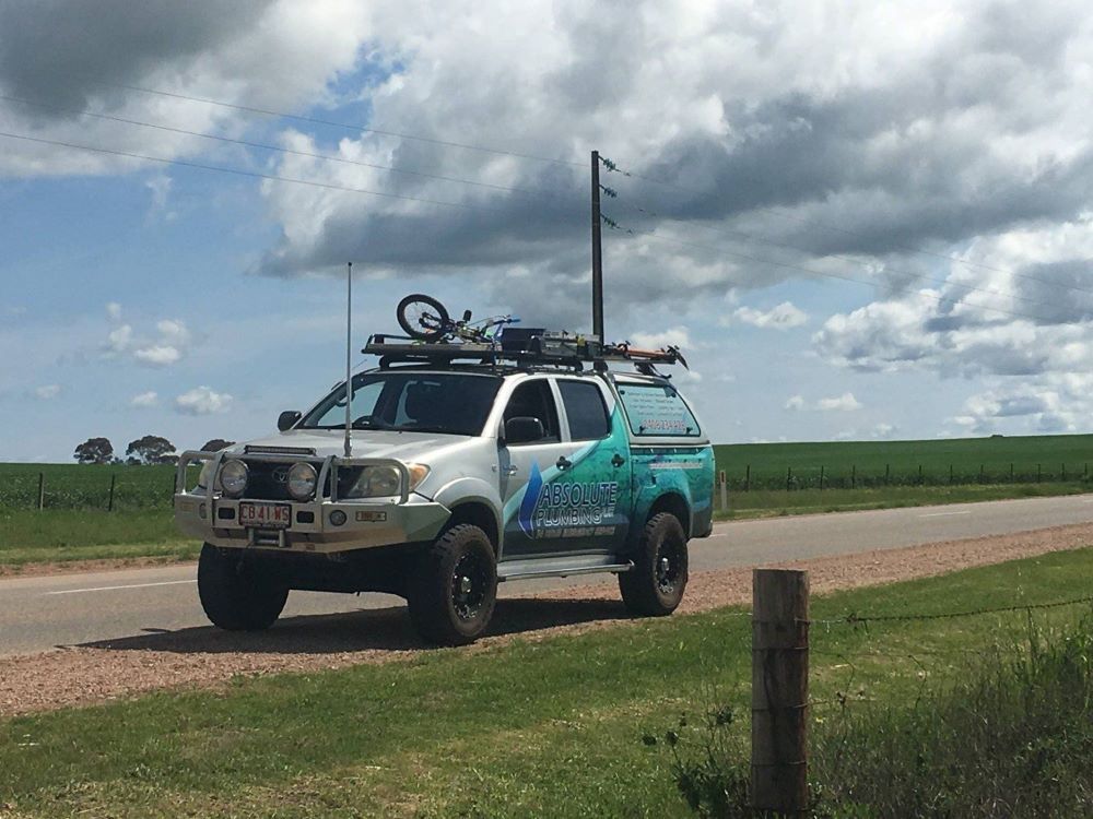 A Truck With a Bike on Top of It is Parked on the Side of the Road — Absolute Plumbing Australia in Darwin Region, NT