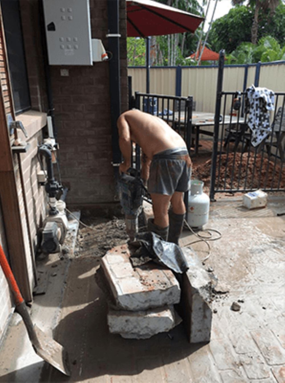 A Man With a Beard is Laying on the Ground Digging a Hole With a Shovel — Absolute Plumbing Australia in Howard Spring, NT