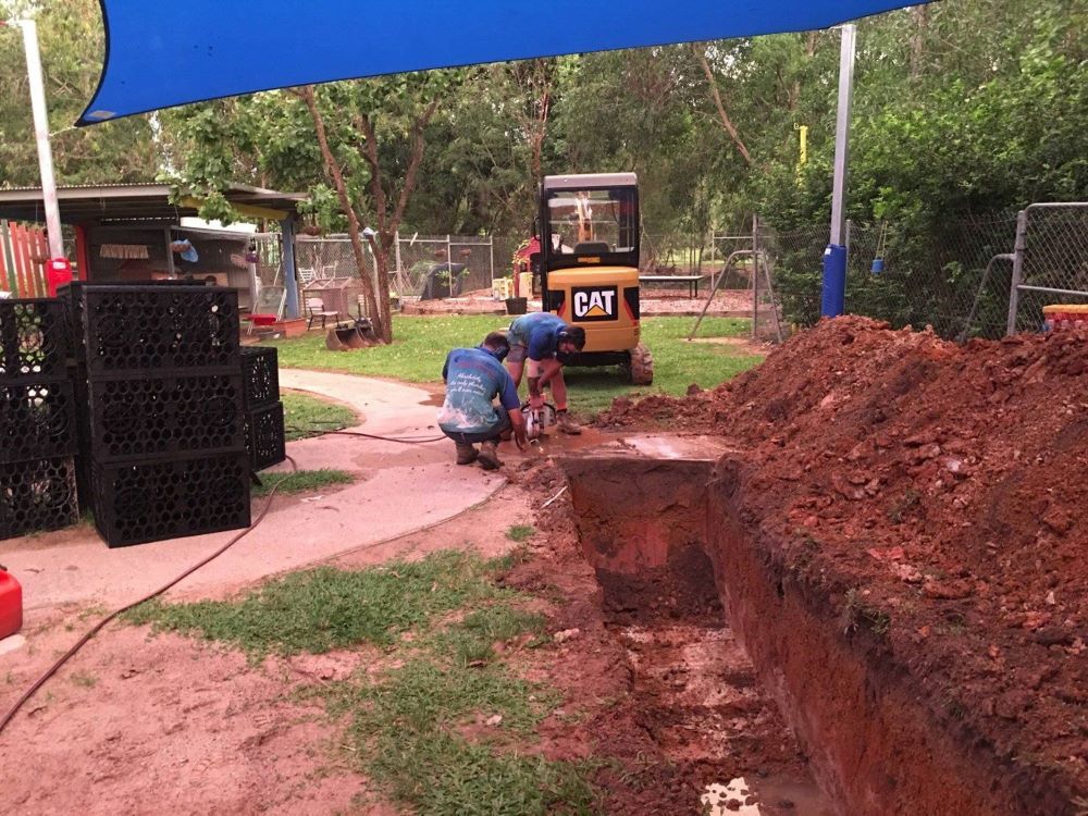 A Group of Men Are Working on a Construction Site With a Cat Bulldozer in the Background — Absolute Plumbing Australia in Howard Spring, NT