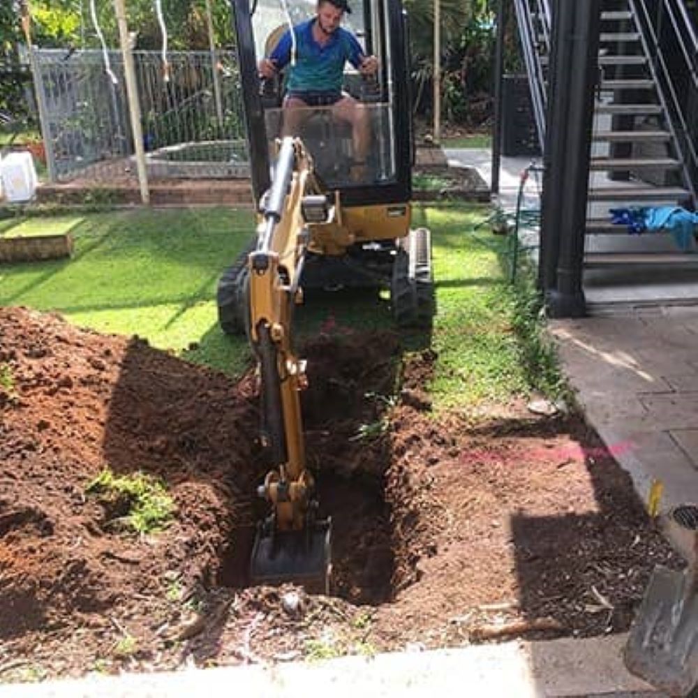 A Man is Driving a Small Excavator in a Yard — Absolute Plumbing Australia in Howard Spring, NT