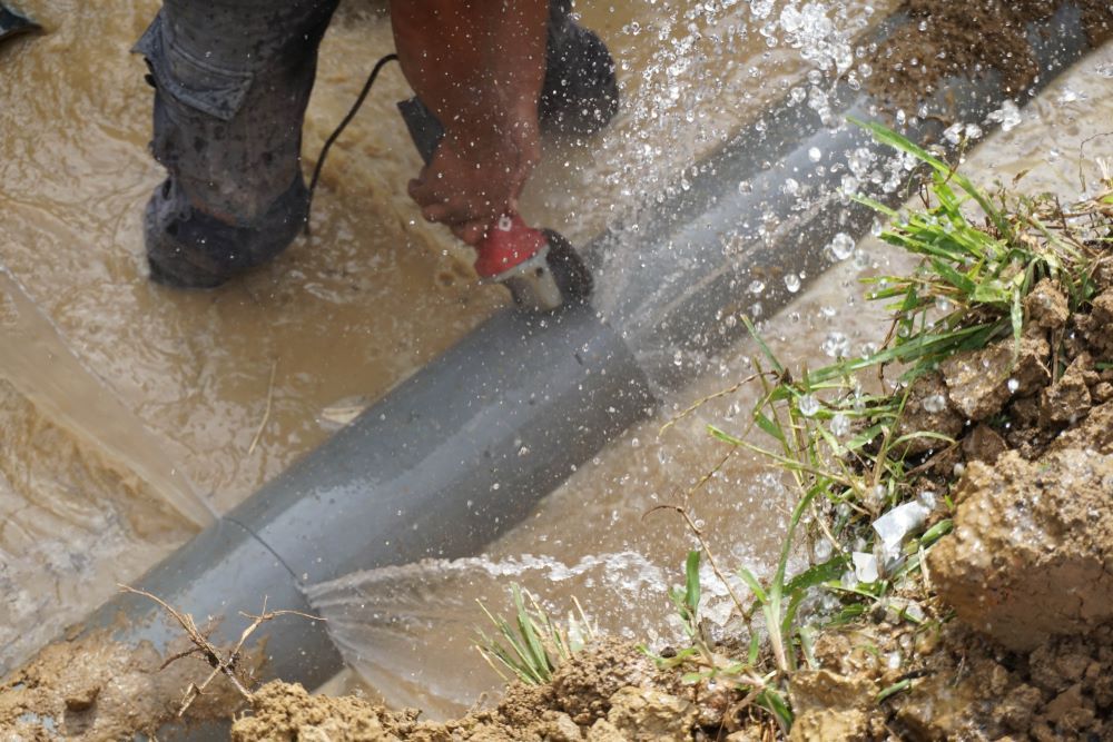A Man is Cutting a Pipe With a Grinder in the Mud — Absolute Plumbing Australia in Humpty Doo, NT