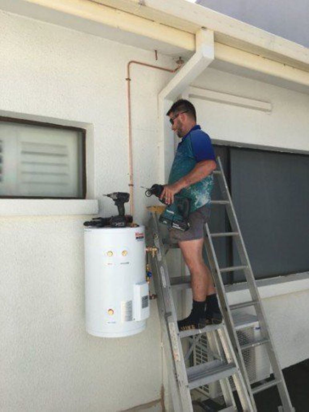 A Man on a Ladder Working on a Water Heater — Absolute Plumbing Australia in Howard Spring, NT