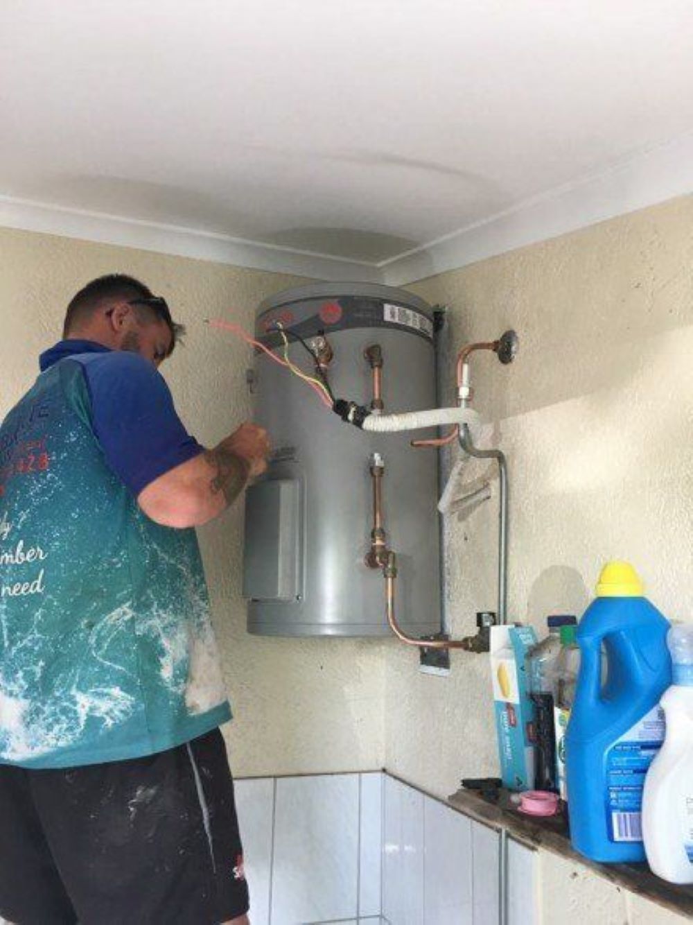 A Man is Fixing a Water Heater in a Bathroom — Absolute Plumbing Australia in Howard Spring, NT