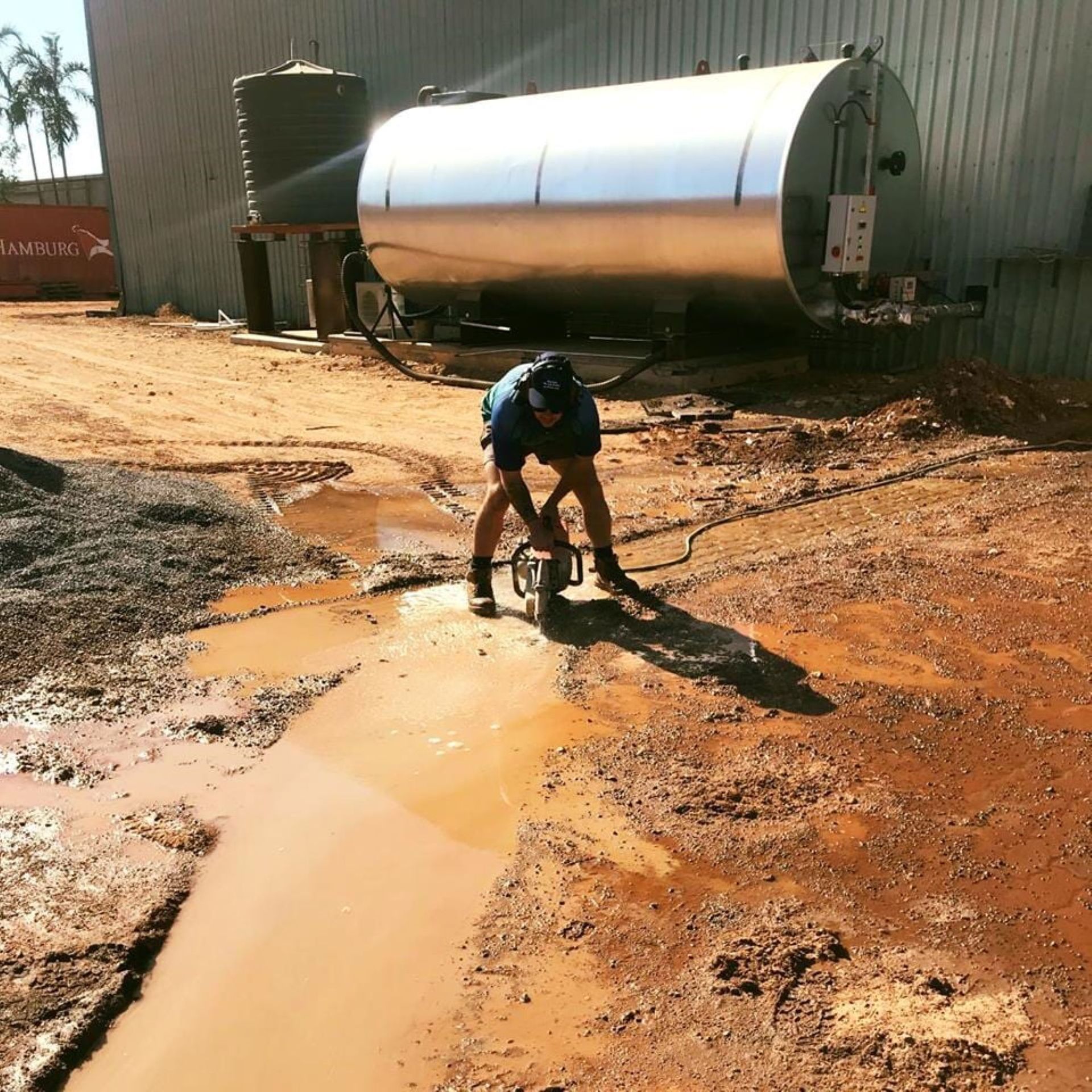 A Man is Standing in a Muddy Area Near a Large Tank — Absolute Plumbing Australia in Nightcliff, NT