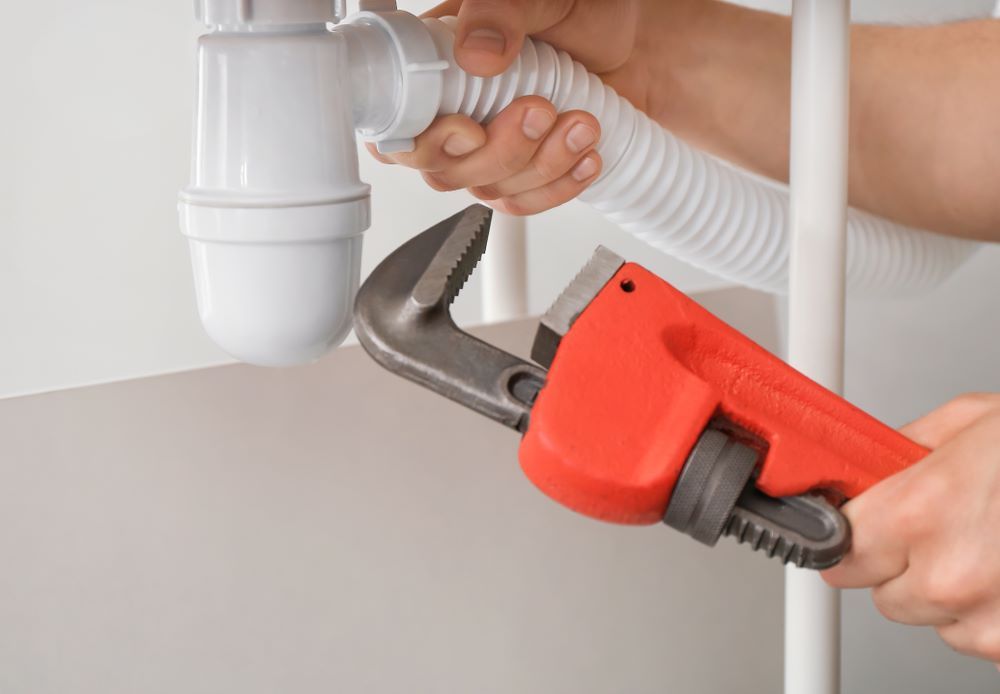 A Person is Fixing a Sink Pipe With a Wrench — Absolute Plumbing Australia in Howard Spring, NT