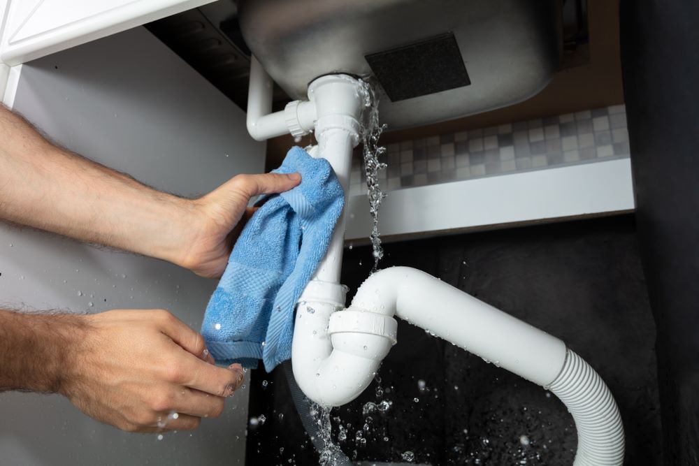 A Person is Cleaning a Leaking Sink Pipe With a Towel — Absolute Plumbing Australia in Palmerston, NT