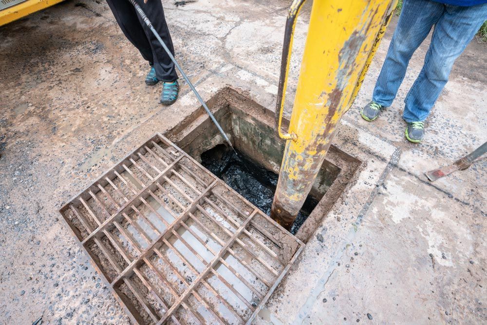 A Manhole Cover is Being Cleaned by a Yellow Excavator — Absolute Plumbing Australia in Palmerston, NT