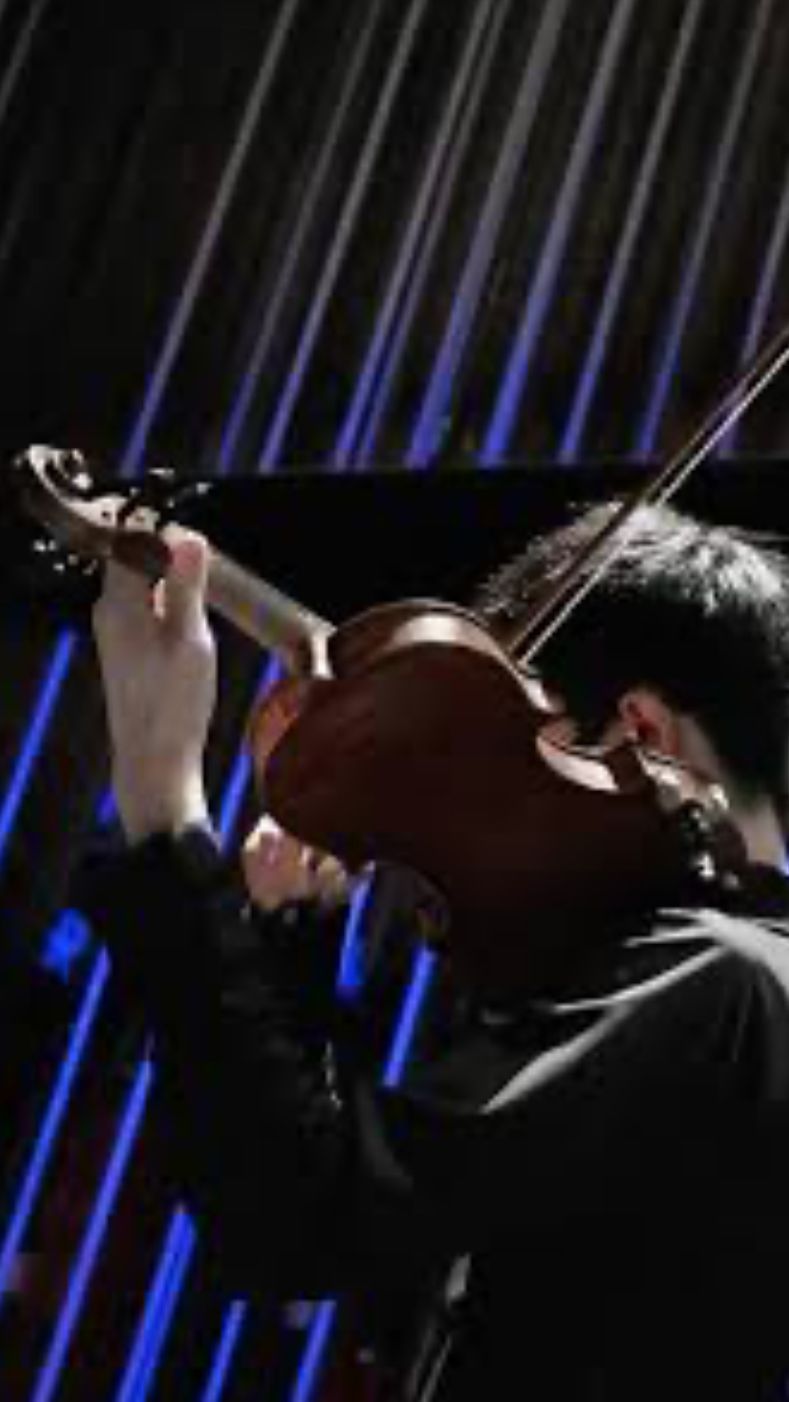 Person playing a violin; illuminated stage with blue lights in the background.