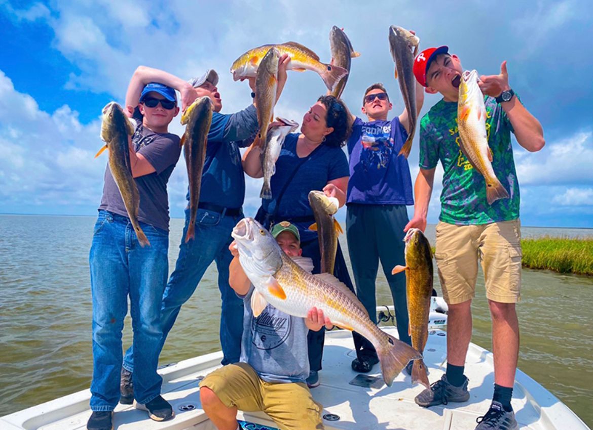 Group on boat holding up freshly caught redfish, smiling in outdoor setting.