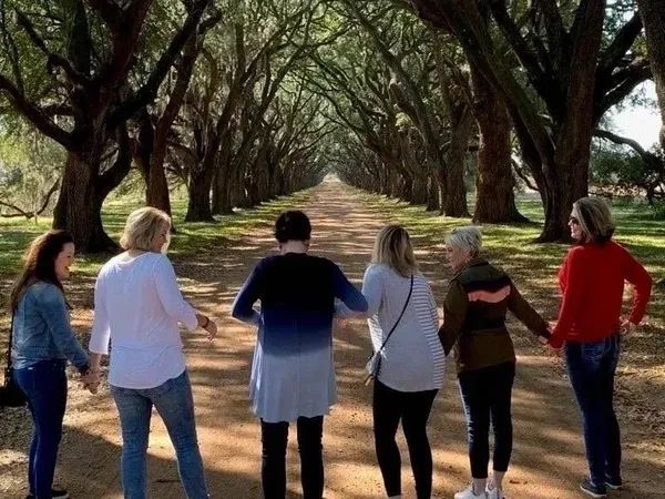 A group of women are standing on a dirt road holding hands.