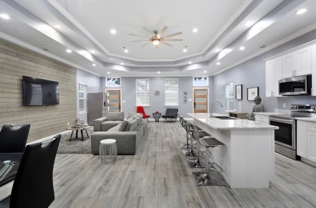 Spacious, open-concept living area with kitchen island, gray flooring, white cabinets, and wood accent wall.