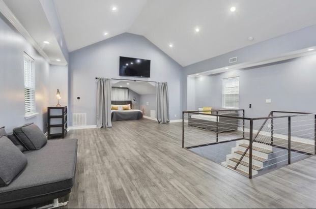 Spacious modern loft with gray walls and wood floors. Includes a sofa, bed area, and a platform bed with stairs.