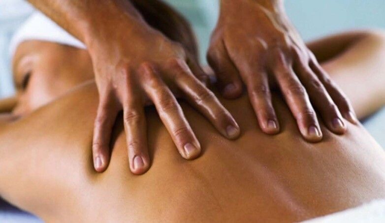 Hands massaging the back of a person lying face down, in a spa setting.