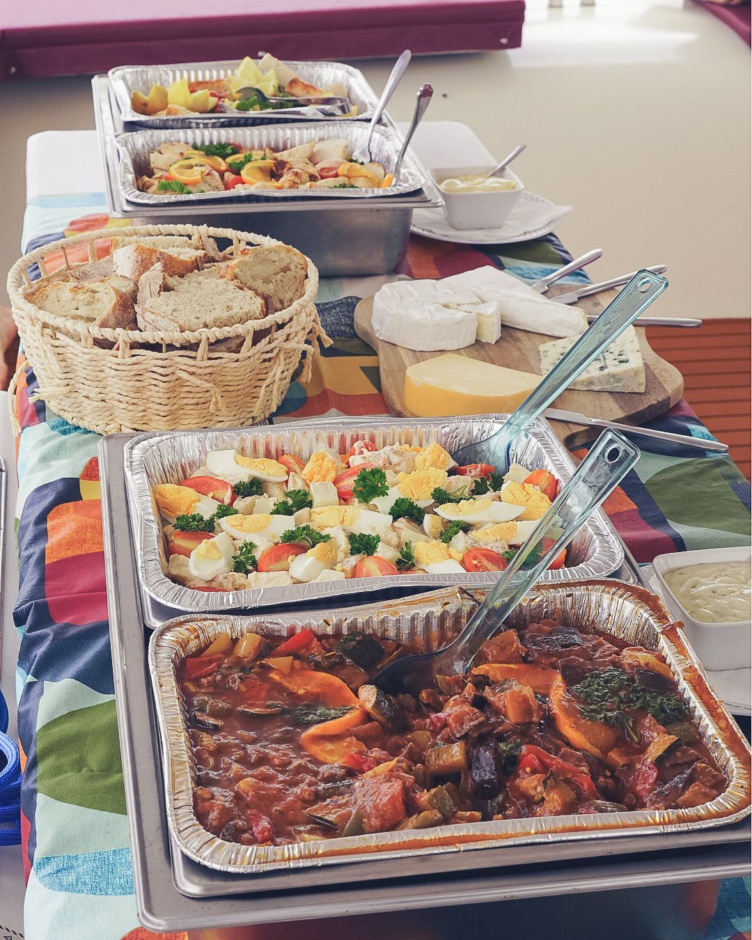 Une table de buffet avec plusieurs plateaux en aluminium contenant de la nourriture, du pain et du fromage.