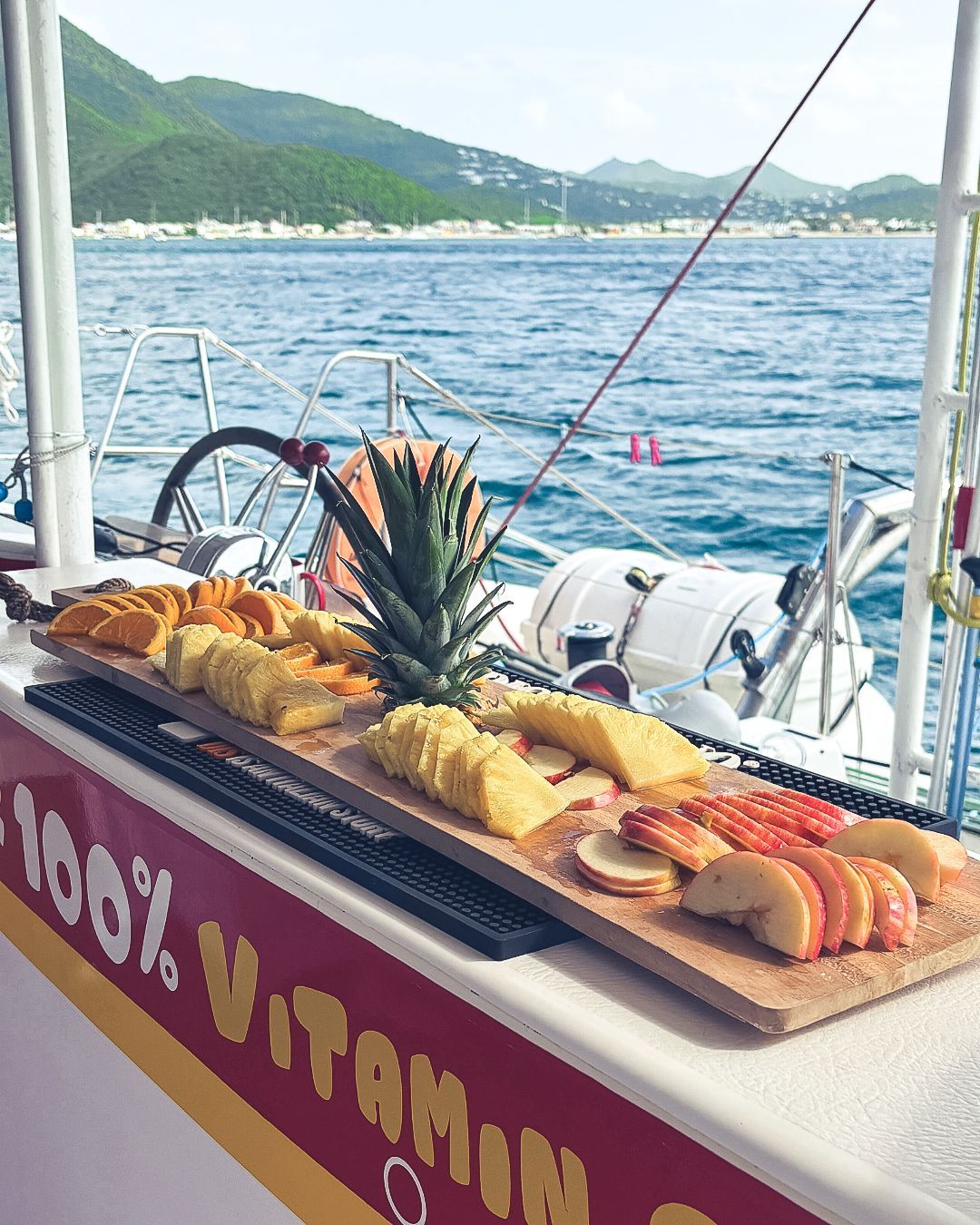 Plateau en bois garni de fruits tranchés, d'ananas, sur un bateau avec vue sur l'océan.
