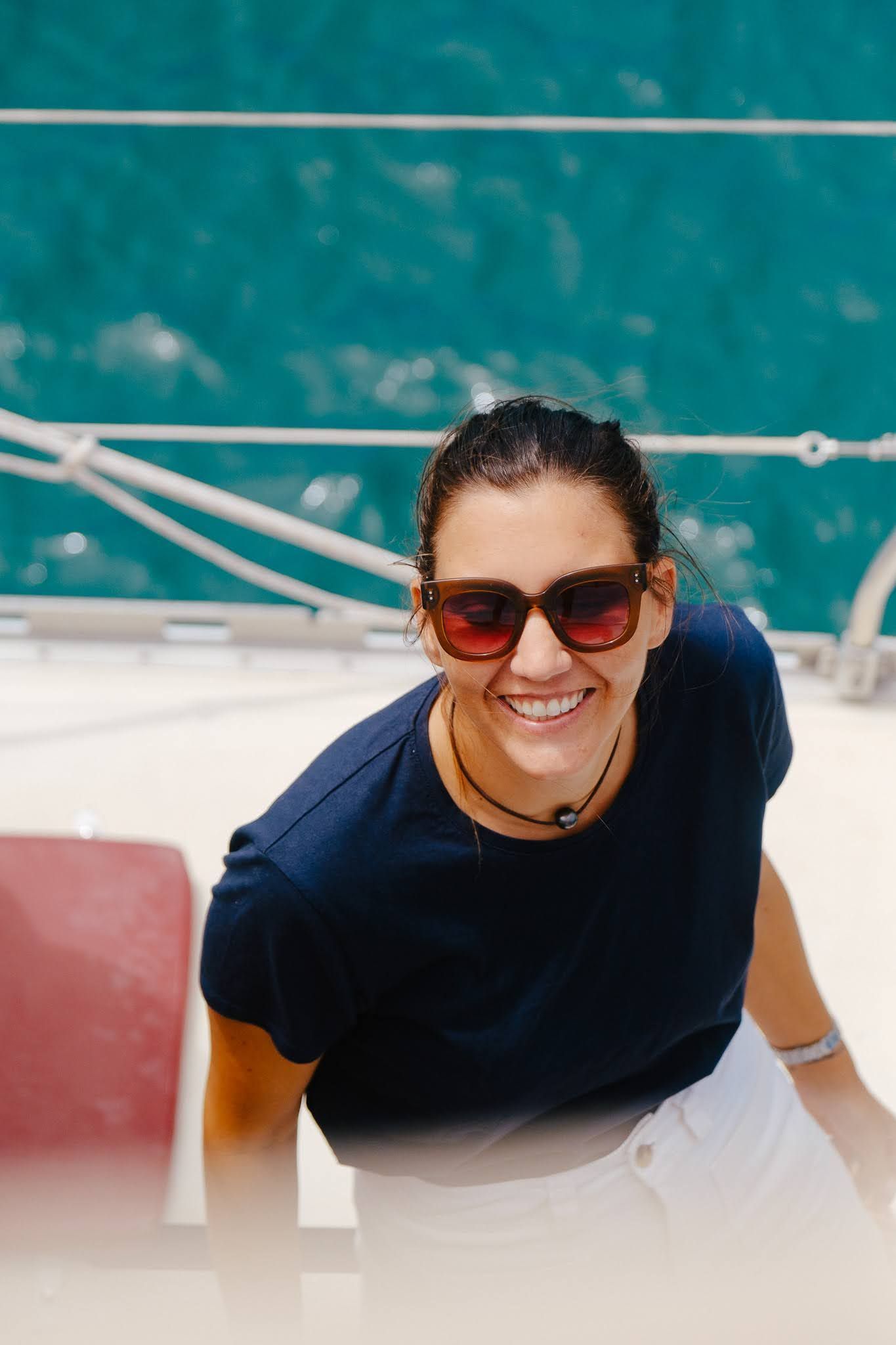 Woman smiling while on phone by the water; wearing a navy shirt and gold bracelet.