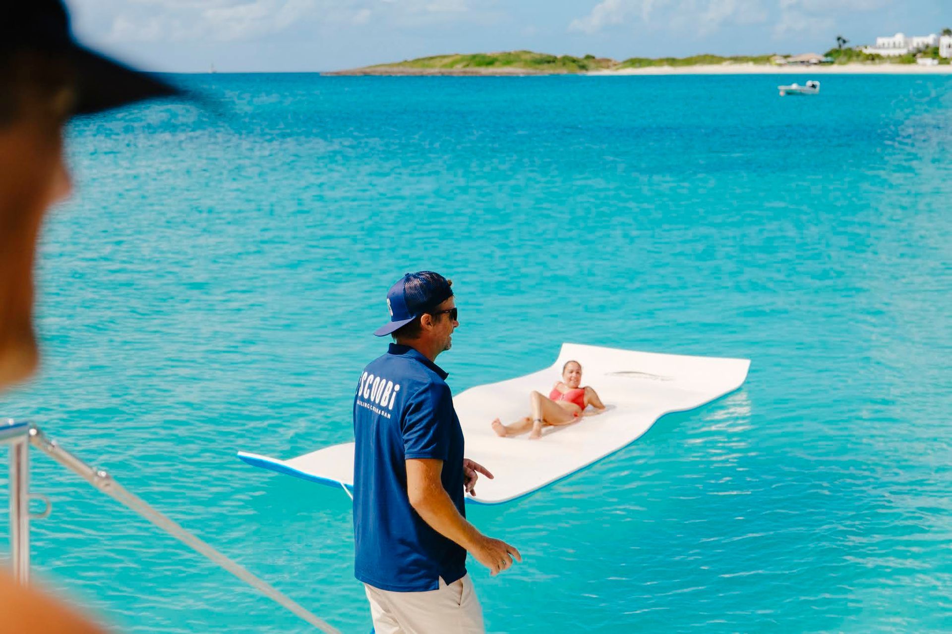 Person on raft in turquoise water, guided by a crew member near a boat; sunny day.