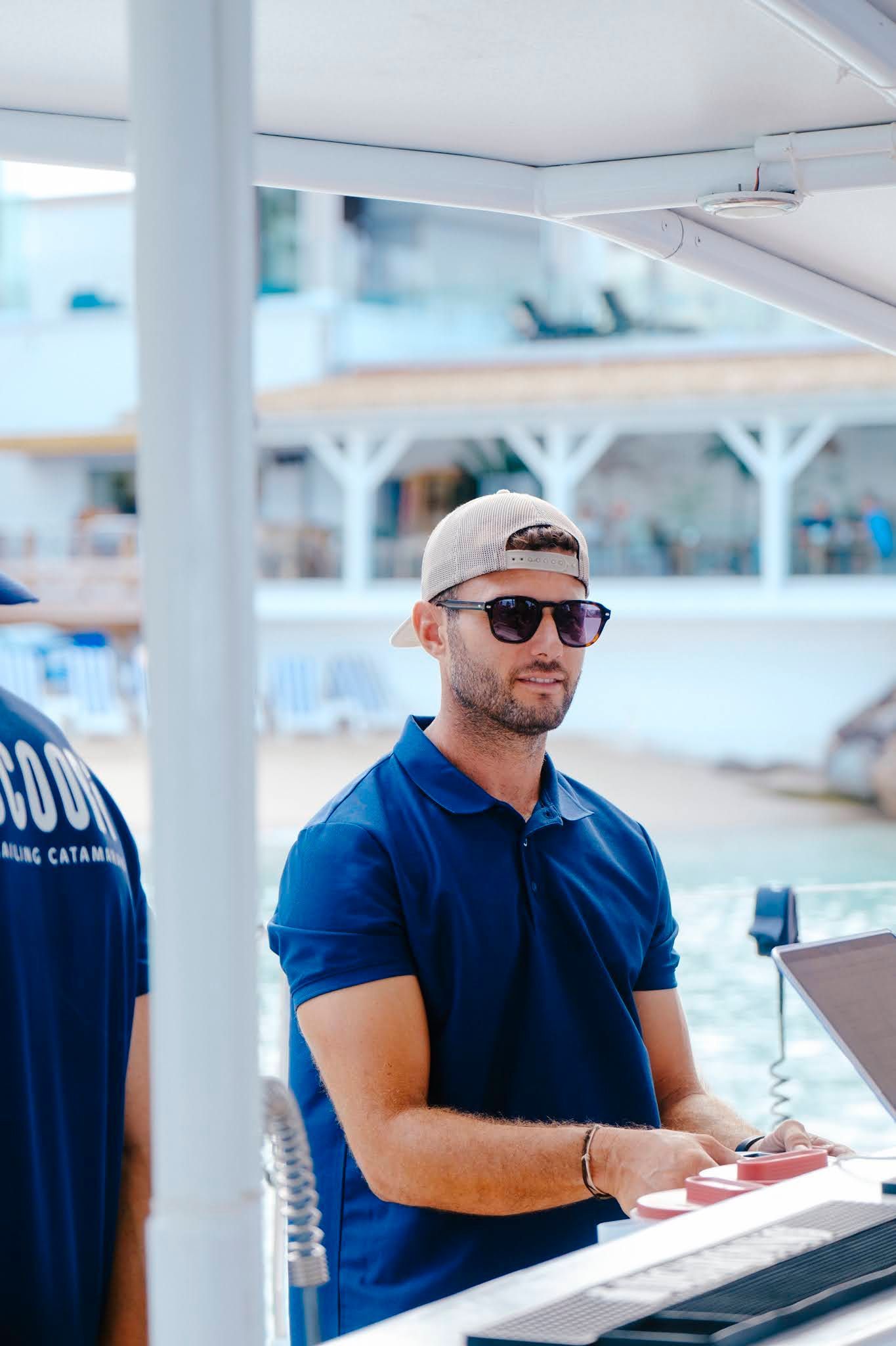 Man in sunglasses and baseball cap plays a keyboard outdoors. Blue shirt, sunny setting.