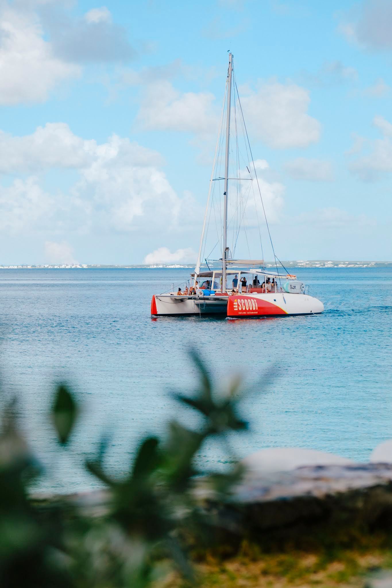 Catamaran sailing on blue water, under a bright, cloudy sky.