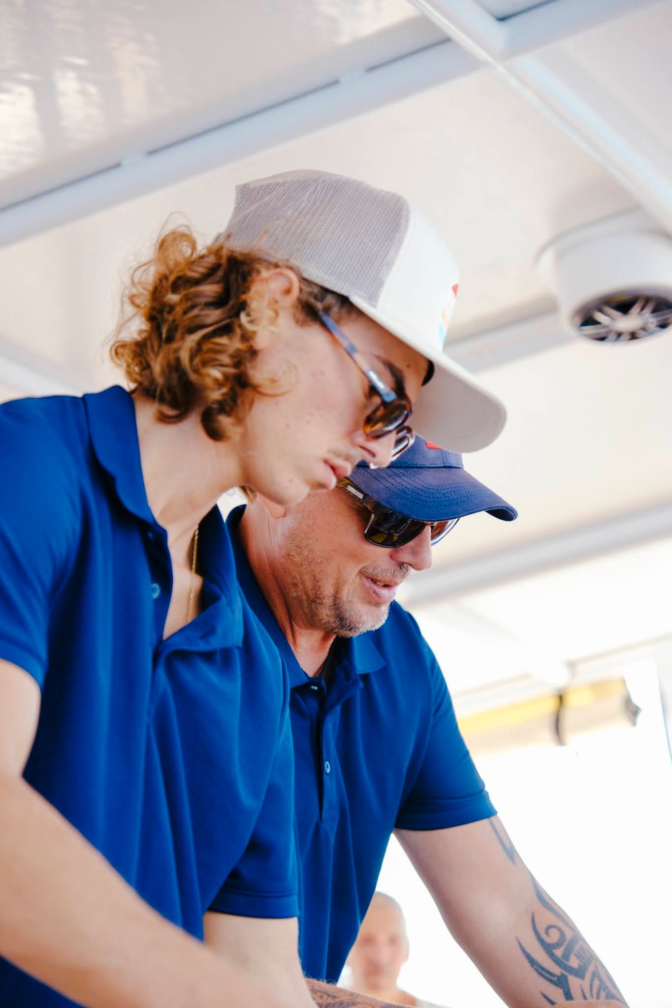 Two people wearing blue shirts and hats, looking down; outside on a boat.