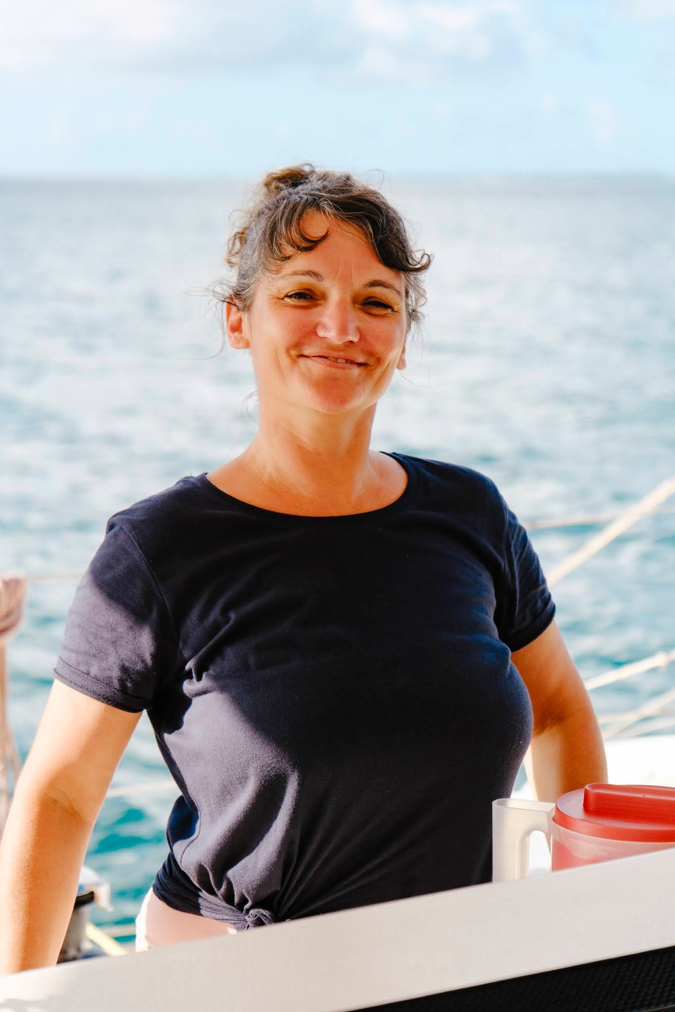 Woman on a boat smiles, ocean and sky in background. She wears a dark shirt.