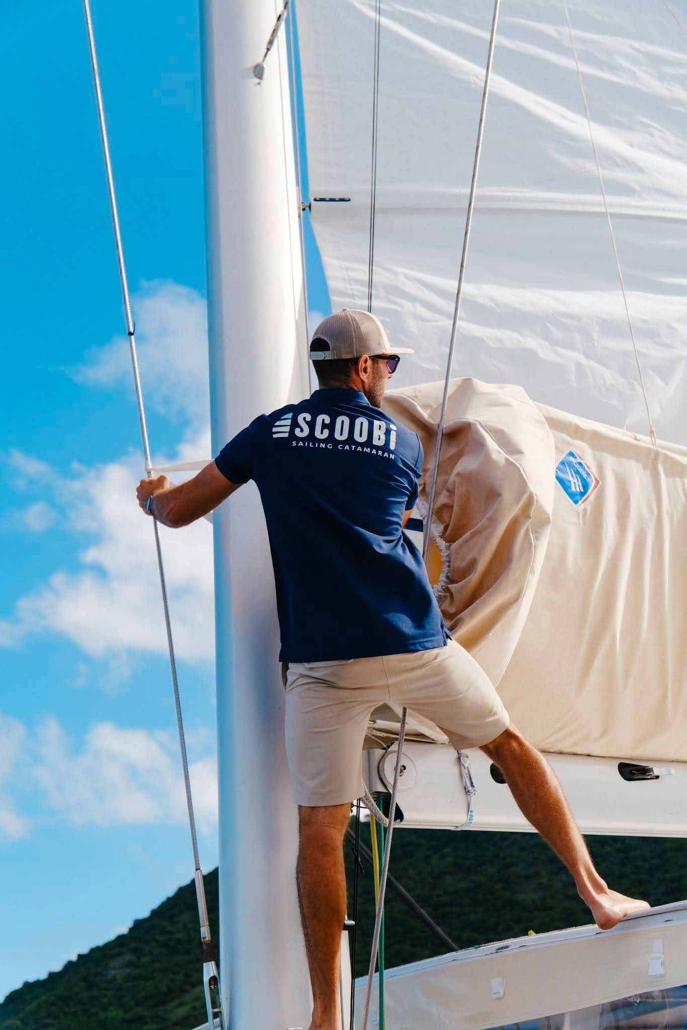 Person on sailboat, holding ropes near a mast, against a blue sky.