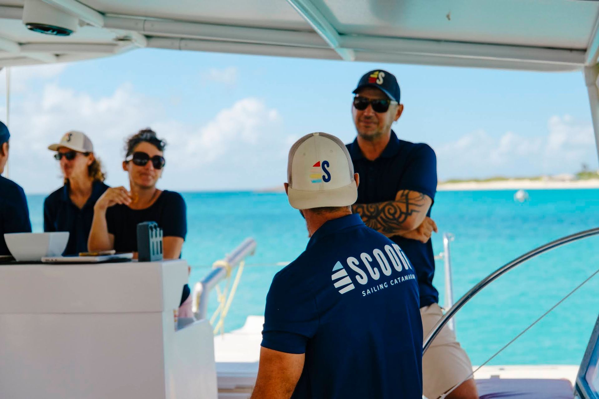 People on a boat looking out at ocean; one wearing a SCOUT hat, others wearing sunglasses.