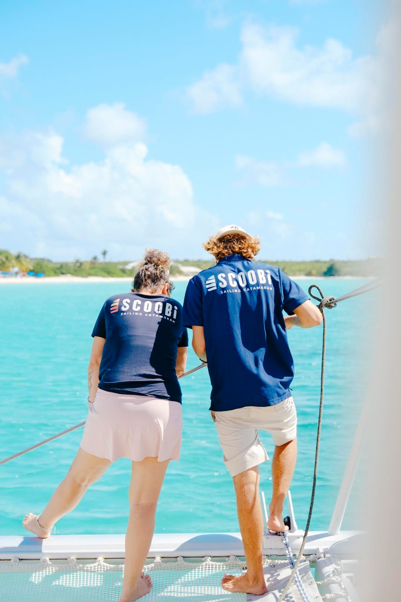 Two people on a boat look out at turquoise water and a beach, wearing blue shirts.