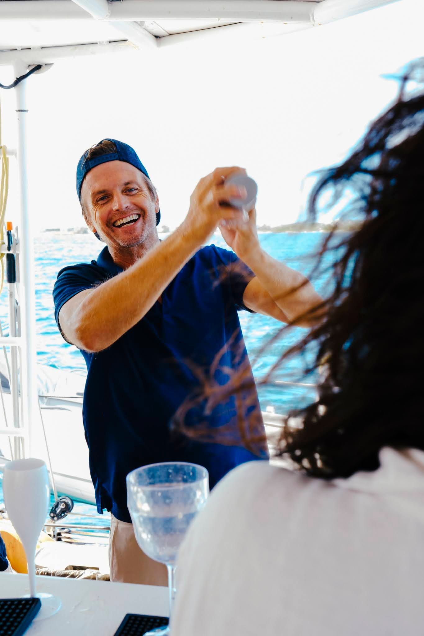 Man claps hands excitedly on boat, facing another person. Blue sky, water visible.