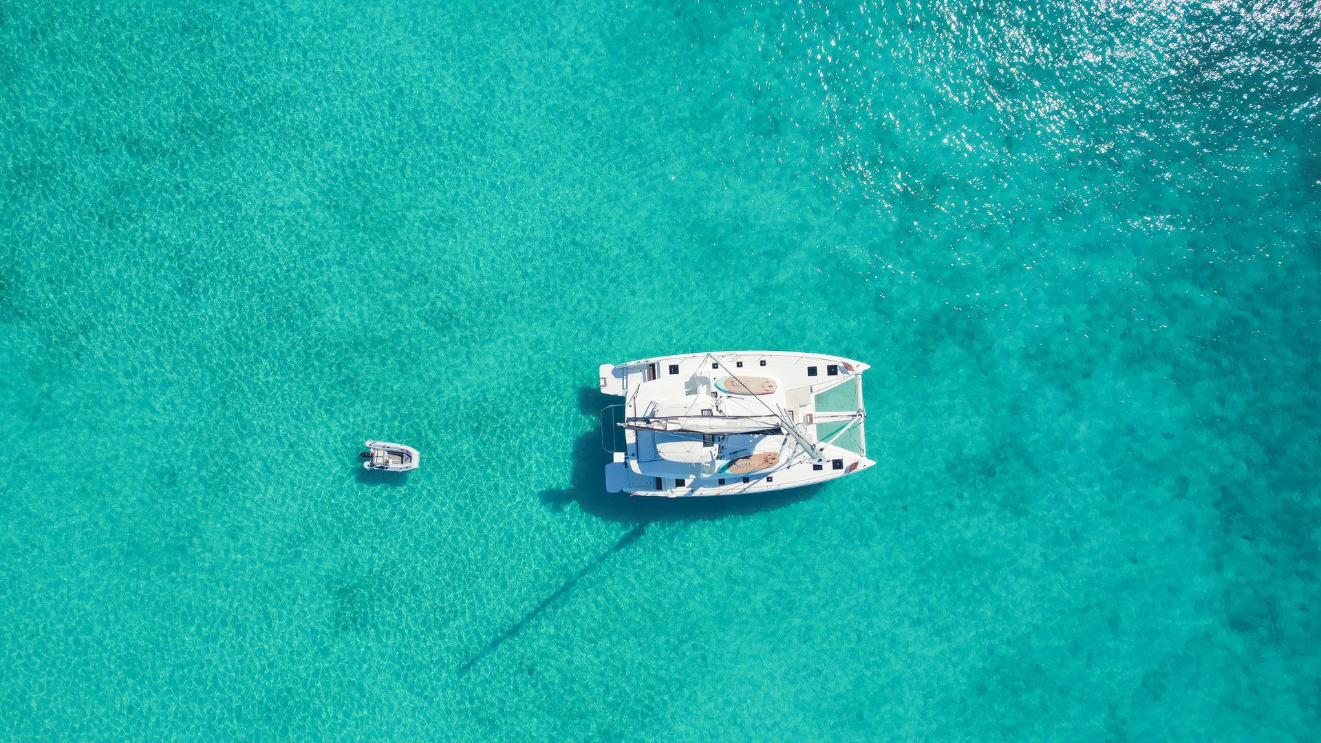 Catamaran and small boat in clear turquoise water.