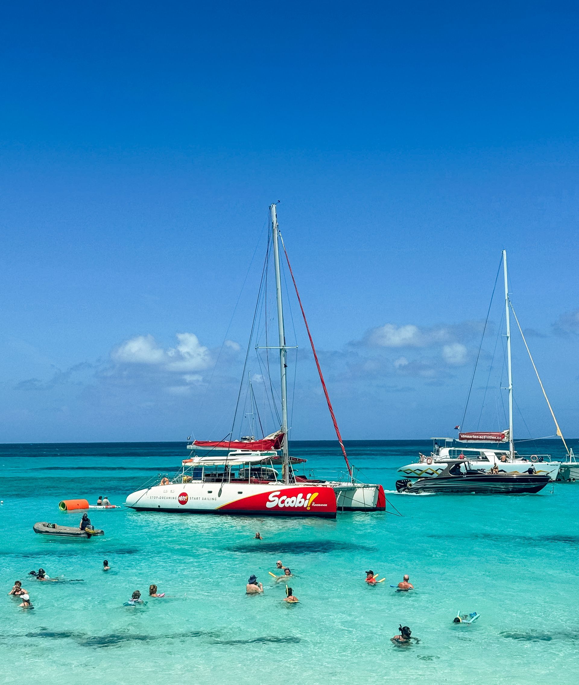 Catamarans anchored in turquoise water with people swimming. Sunny day, blue sky.